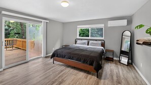 A bedroom with a bed, a sliding glass door to a deck, a window, and a wall-mounted air conditioner.