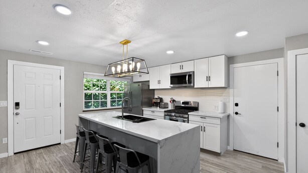 A modern kitchen with a central island, bar stools, white cabinetry, and recessed lighting.
