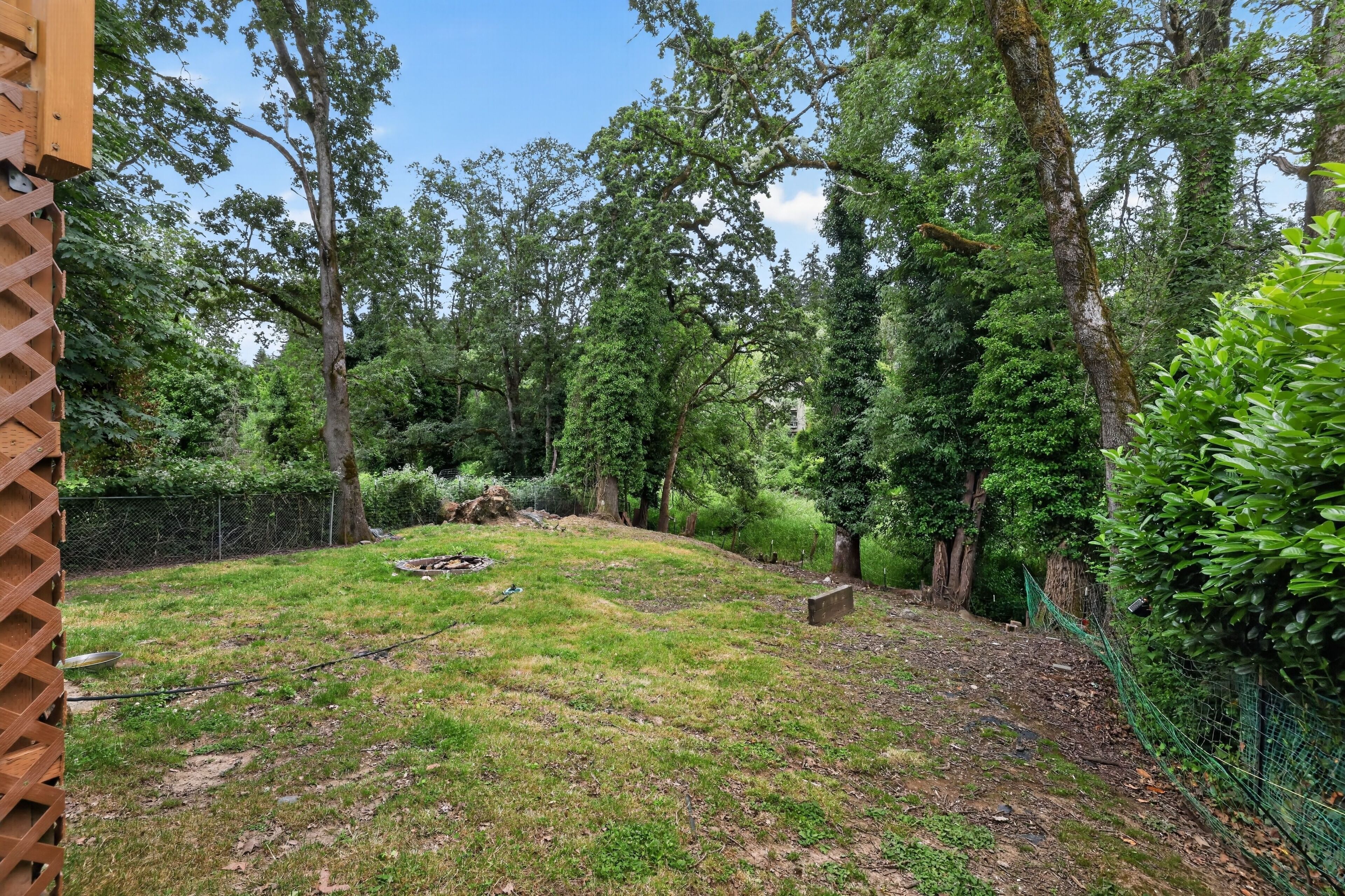 A garden with a wooden fence, trees, and a grassy area.