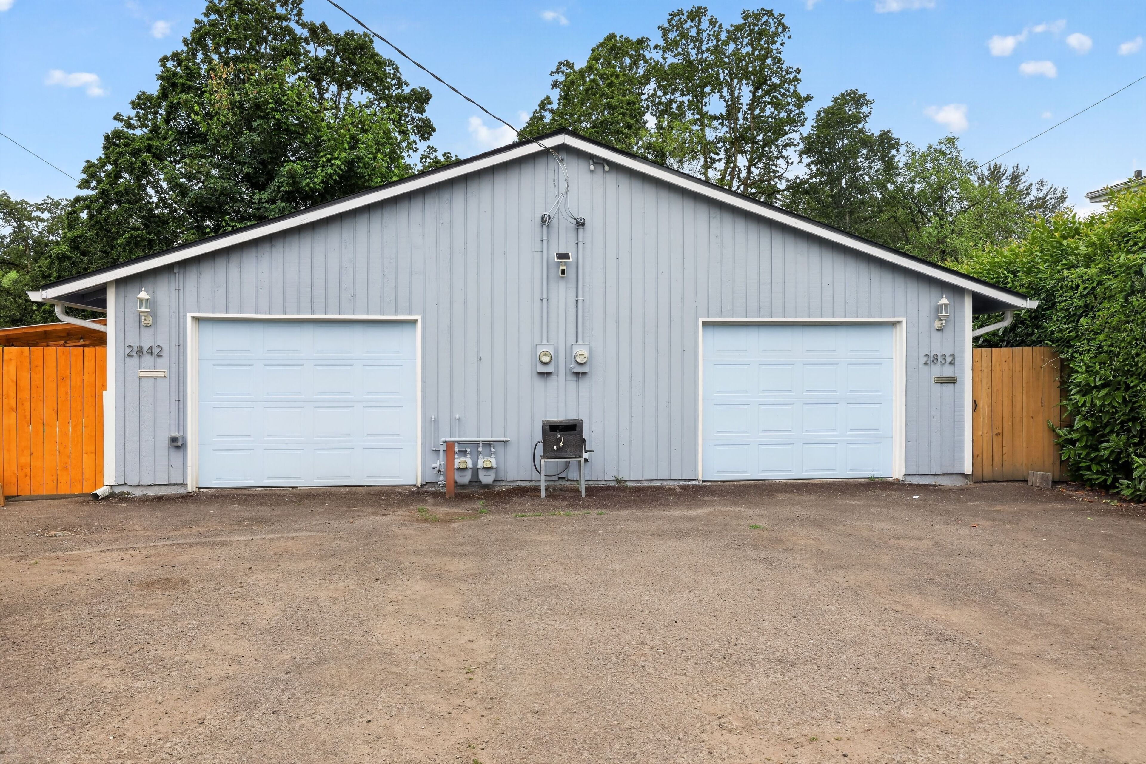 A two-story building with two garage doors, a small utility shed, and a wooden fence.