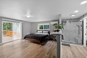 Un dormitorio moderno con cama, mesita de noche, planta en maceta, cabina de ducha de vidrio y vistas al exterior.