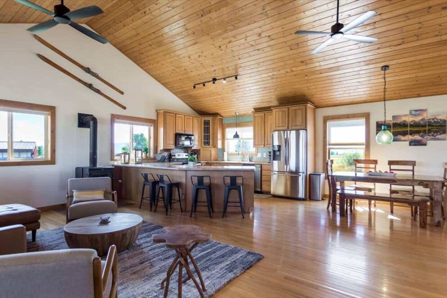Une cuisine spacieuse avec des meubles en bois, un îlot central doté de tabourets de bar, un coin repas avec une table et des chaises en bois, et un ventilateur de plafond.
