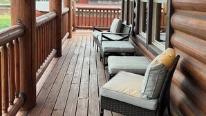 Een houten terras met een leuning, twee rieten stoelen met kussens en uitzicht op het landschap.