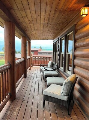 Una terraza de madera con barandilla, dos sillas de mimbre con cojines y vistas al paisaje.