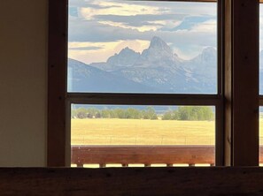 Ein Fenster mit Blick auf ein Gebirge und ein Feld.