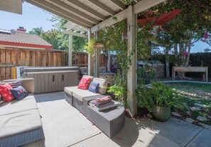 Un patio techado con una zona de estar integrada, un jacuzzi y un jardín con plantas en macetas.