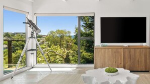 Ein modernes Wohnzimmer mit Teleskop, großen Fenstern, einem Flachbildfernseher und einer Holzschrank.