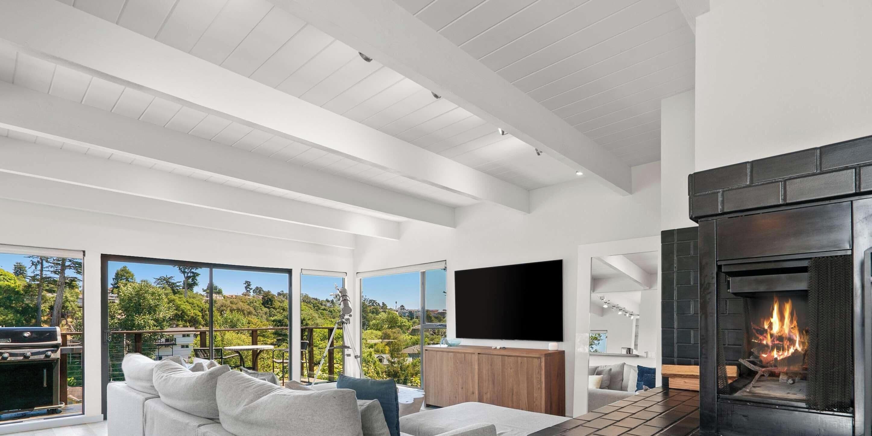 A modern living room with a fireplace, a large TV, and a balcony with a view of the hills.