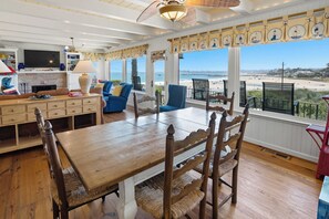 Ein Essbereich mit Holztisch und Stühlen, einem Fernseher und Blick auf den Strand.