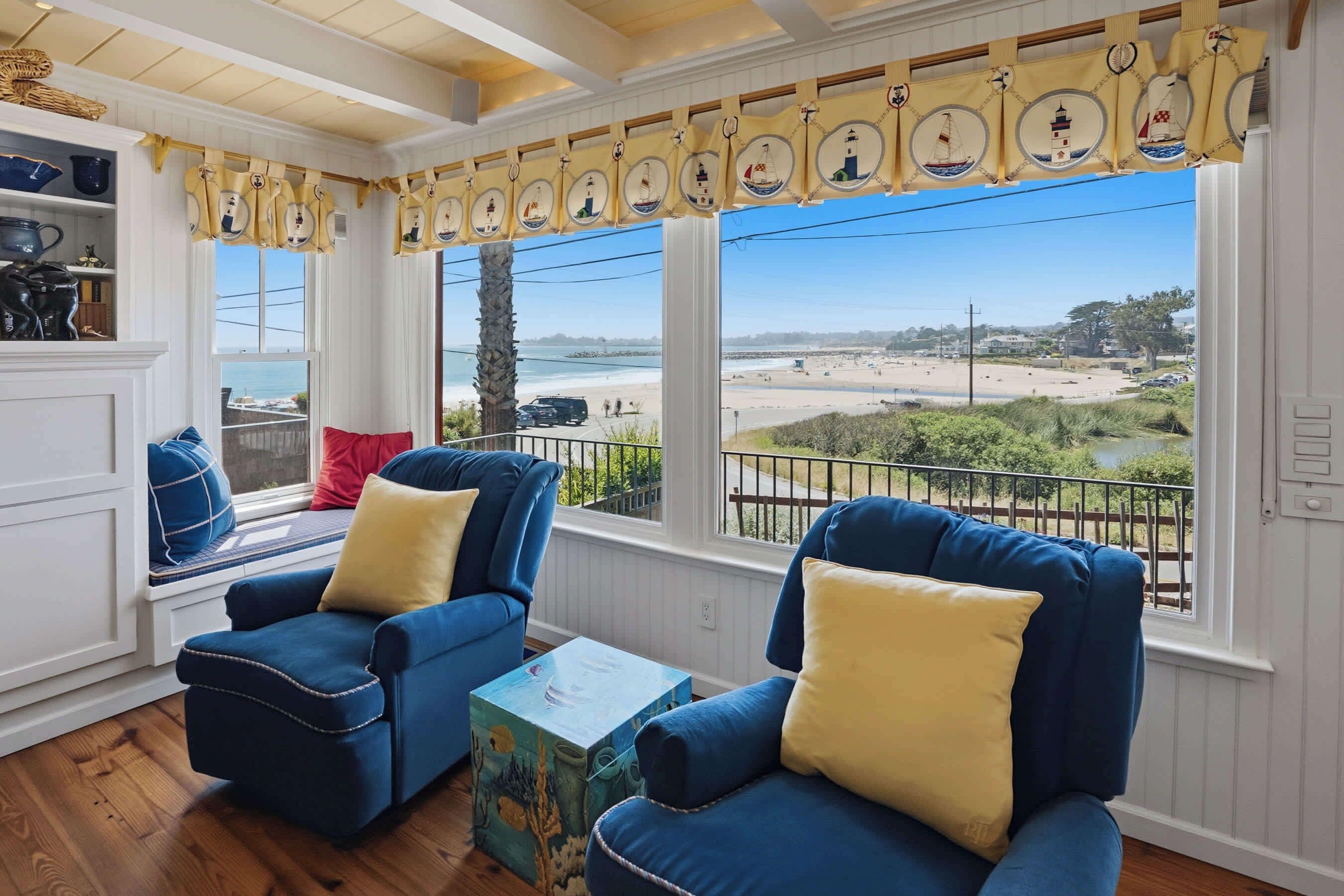 A room with two blue armchairs, a small table, and a view of the beach.