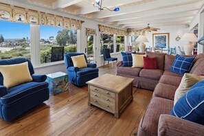 Ein Wohnzimmer mit Holzboden, blauen und braunen Sofas, einem Beistelltisch und Blick ins Freie.