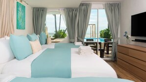 Habitación de hotel con cama, televisión, vista al océano y balcón con mesa y sillas.