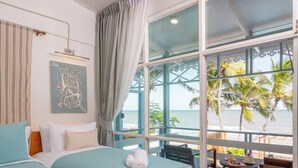 Un dormitorio con dos camas, vista a la playa y un balcón con mesa y sillas.