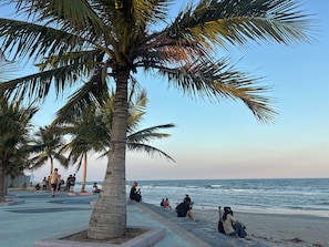 Een promenade aan het strand met palmbomen en mensen die op het voetpad zitten.
