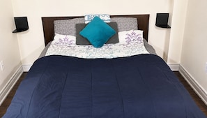 A bed with a dark blue bedspread, a wooden headboard, and multiple pillows with various patterns. - Affordable Spacious Private Suite| Ensuite Bath | Free Parking | Pearson Airport (Mississauga)
