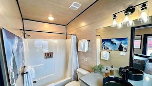 A modern bathroom with a bathtub, toilet, and sink, featuring wooden paneling and a large mirror.