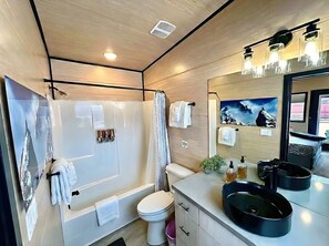 Ein modernes Badezimmer mit einer Badewanne, Toilette und Waschbecken, mit Holzvertäfelung und einem großen Spiegel.