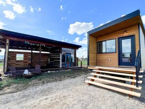 A cabin with a wooden exterior, a porch with chairs, and a gravel ground.