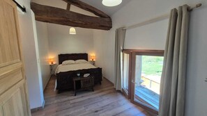Ein Schlafzimmer mit einem hölzernen Bett, Nachttischlampen, einem kleinen Tisch und einer Schiebeglastür zum Balkon.
