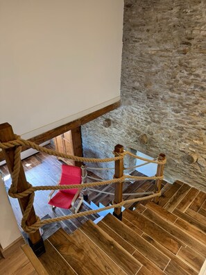 Eine Holztreppe mit einer Seilsperre, einer Steinmauer und einem roten Stuhl im Hintergrund.