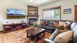 Una sala de estar con chimenea, un televisor de pantalla plana grande, un sofá de cuero y un mueble de madera para entretenimiento.