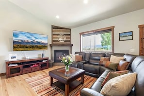 A living room with a fireplace, a large flat-screen TV, a leather sofa, and a wooden entertainment unit. - Targhee & Teton Getaway (Driggs)
