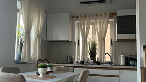 Une cuisine moderne avec des meubles blancs, une table à manger avec des chaises et une fenêtre avec des rideaux.