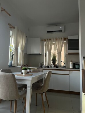 Una cucina moderna con mobili bianchi, un tavolo da pranzo con sedie e una finestra con tende.