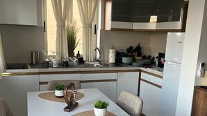Une cuisine moderne avec des meubles blancs, une table à manger agrémentée de sets de table beiges et un îlot central orné d’une plante en pot.