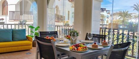 Un coin repas avec une table dressée pour six personnes, entourée de chaises, et donnant sur un balcon.