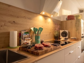 Una cocina moderna con armarios de madera, horno empotrado y una encimera con carne cruda y utensilios de cocina.