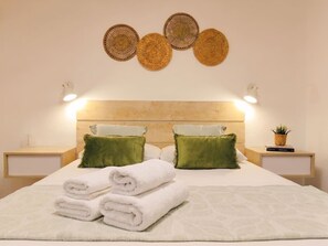 Una cama bien hecha con sábanas blancas, dos almohadas verdes y un cabecero con diseño tejido.
