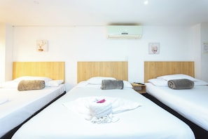 Habitación de hotel con dos camas, cabecero de madera, aire acondicionado de pared y una mesita con lámpara.