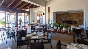 Un'ampia sala da pranzo con diversi tavoli e sedie, un caminetto e grandi finestre che lasciano entrare molta luce naturale.