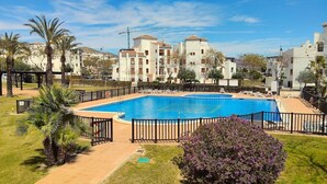 Una piscina circondata da una recinzione, con palme e un edificio sullo sfondo.
