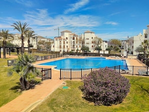 A swimming pool surrounded by a fence, with palm trees and a building in the background. - Pool & Golf View Residence | El Valle, Murcia (Murcia)