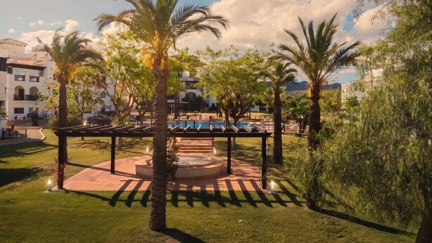 Un cortile con palme, una fontana circolare e una zona piscina.