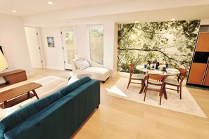 Ein modernes Wohnzimmer mit einer Couch, einem Esstisch, Stühlen und einem großen Fenster.