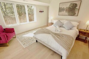 Ein Schlafzimmer mit einem Bett, Nachttischen, einem Fenster, einem rosa Sessel und einem Teppich.