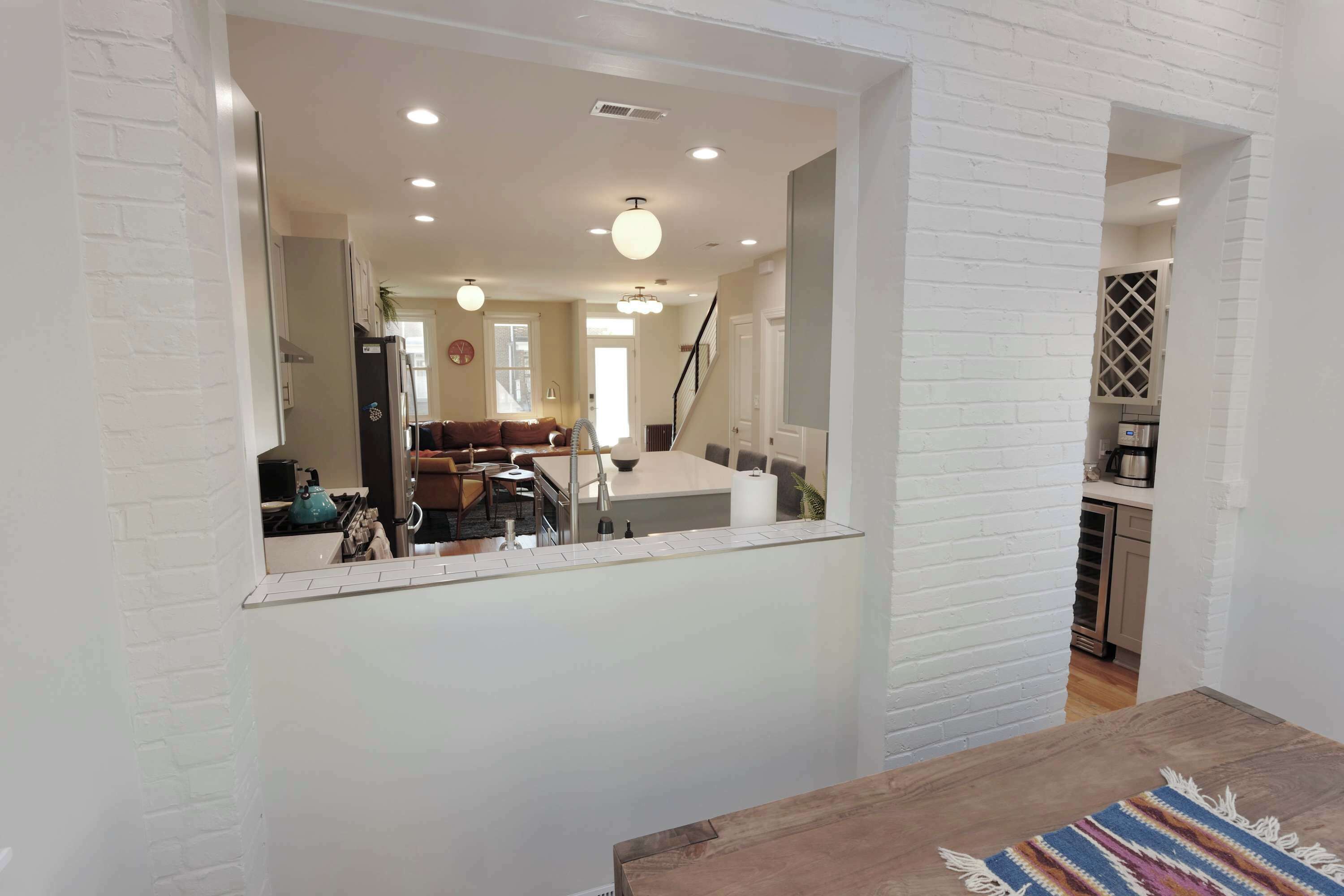 A modern interior with a kitchen, dining area, and living room, featuring white brick walls and recessed lighting.