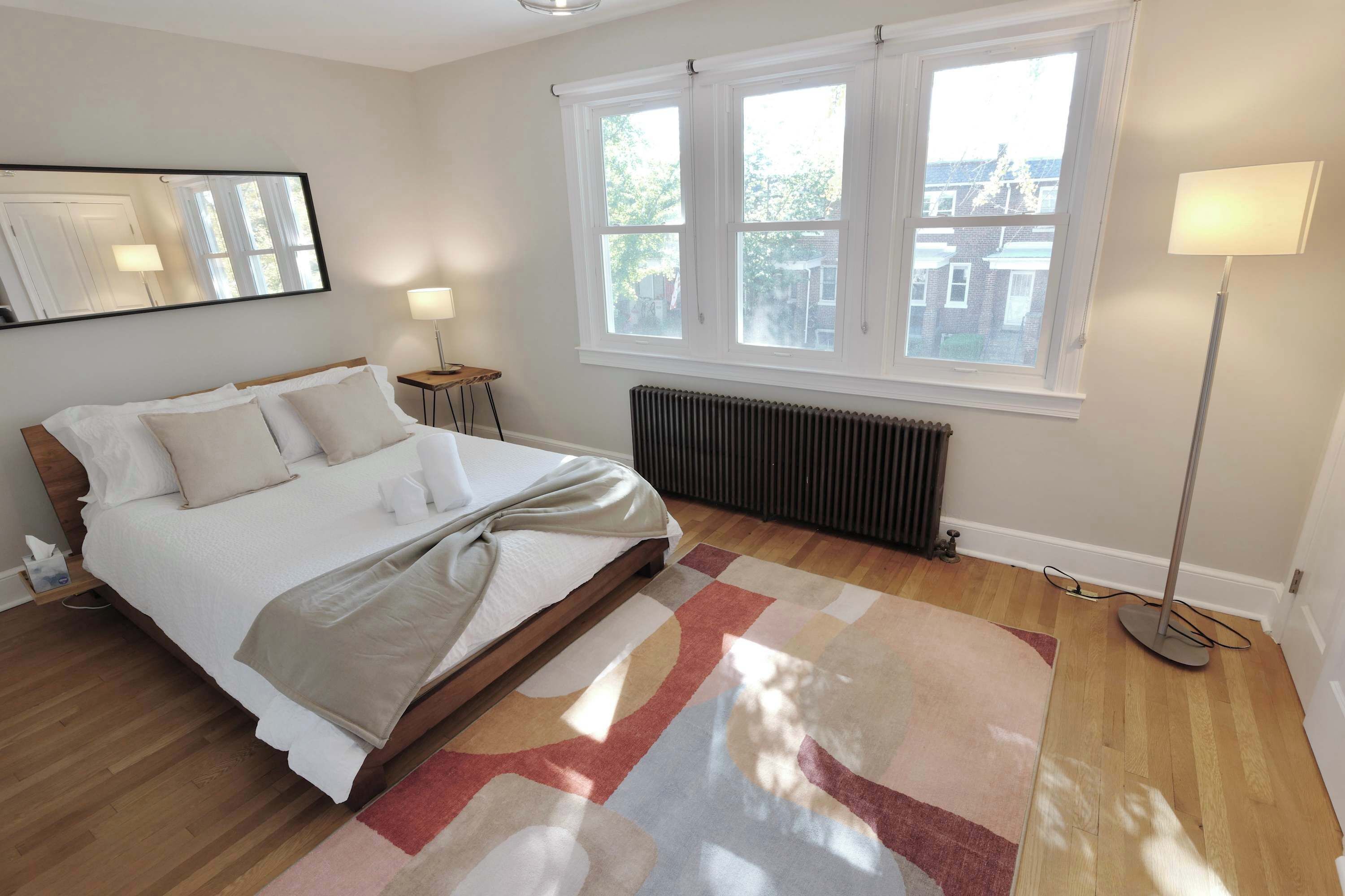 A bedroom with a bed, a radiator, a window, and a floor lamp.