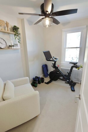 Ein Zimmer mit Deckenventilator, Laufband, weißem Sofa, einer Uhr und einem Fenster mit Blick.
