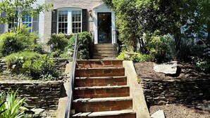 A two-story house with a brick staircase leading to a front door, surrounded by greenery and a stone wall. - 'Book Hill' Georgetown House, Walkable with Garage (Washington)