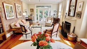 A spacious living room with a fireplace, a dining area with a vase of roses, and a brick wall with framed art. - 'Book Hill' Georgetown House, Walkable with Garage (Washington)