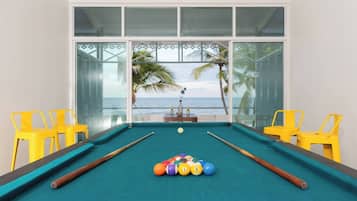 A pool table with balls, yellow chairs, and a view of the ocean through large windows.