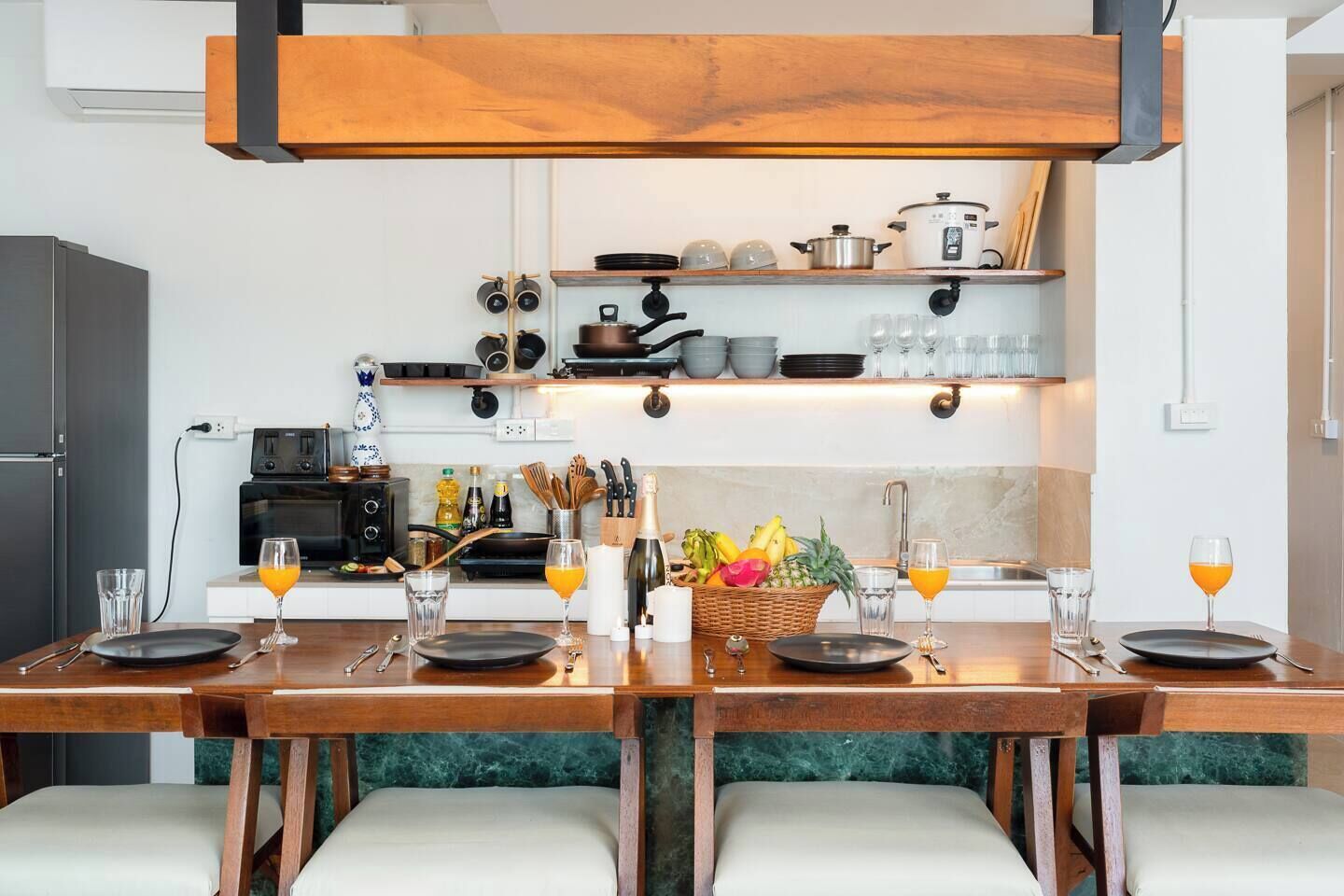 A modern kitchen with a dining table set for two, equipped with a stove, oven, and various kitchen utensils.