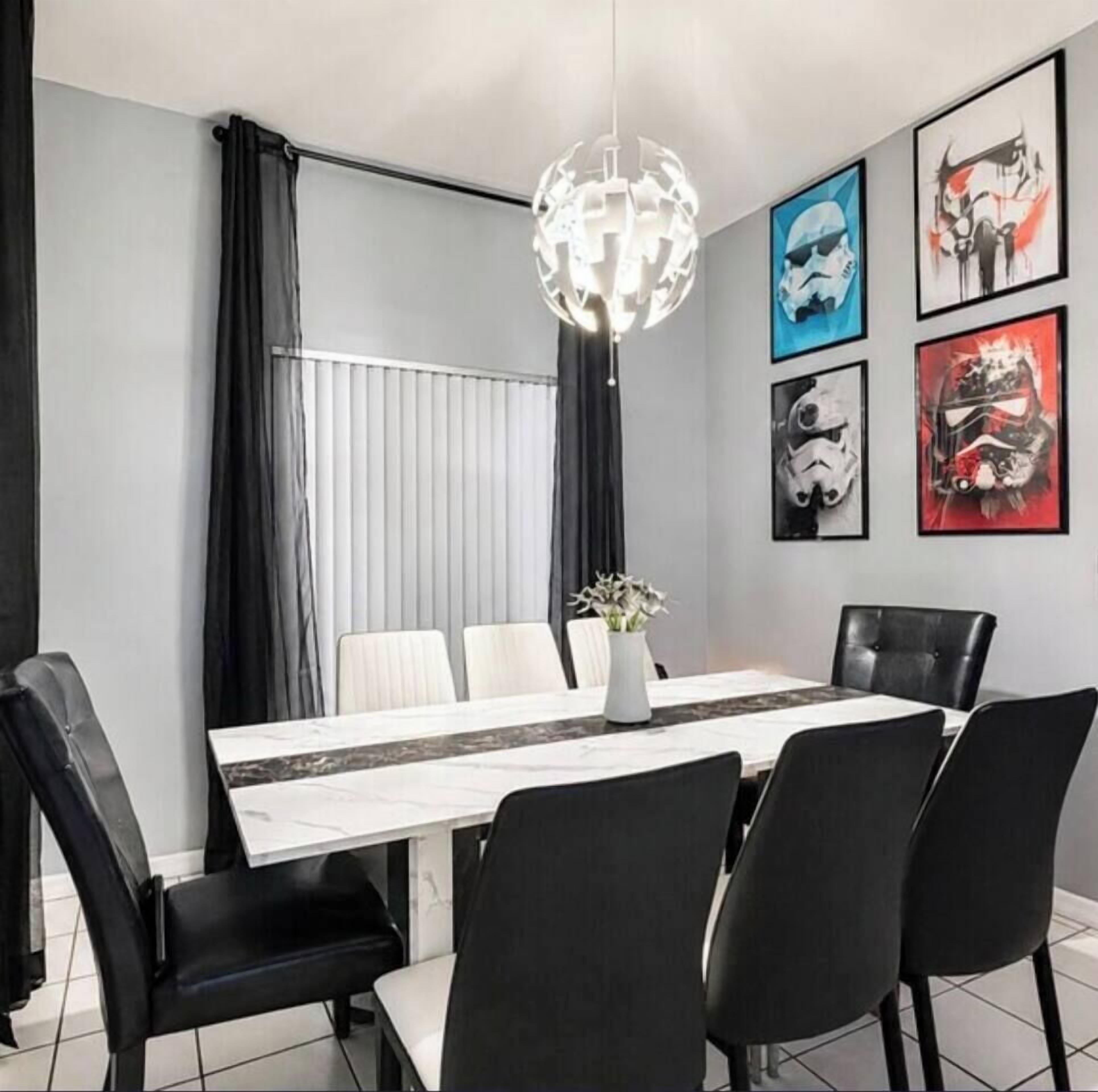 Een eethoek met een witte tafel, zwarte stoelen, een vaas met bloemen en Star Wars-kunstwerken aan de muur.