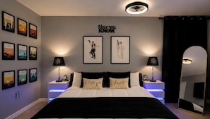 Ein Schlafzimmer mit einem Bett, zwei Nachttischen, Wandbildern, einem Deckenventilator und einem Spiegel.