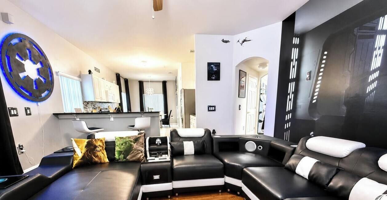 A modern living room with a sectional sofa, a treadmill, and a wall-mounted circular light fixture.