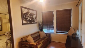 Un salon avec un canapé en bois, un tableau encadré au mur, une fenêtre avec des stores et une lampe.